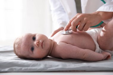 Klinikteki masada steteskopla bebeği muayene eden çocuk doktoru.
