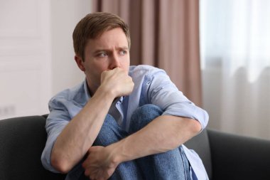 Evdeki koltukta paranoyadan muzdarip korkmuş bir adam.