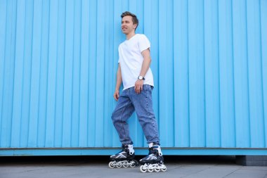Açık mavi duvarın yanında patenli mutlu genç adam