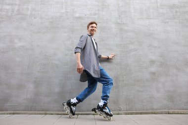 Dışarıda gri duvarın yanında kayan mutlu genç adam.