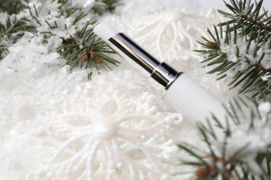 Nemlendirici dudak kremi, Noel dekorasyonu ve yapay kar üzerindeki köknar ağacı dalları, yakın plan. Kış bakımı