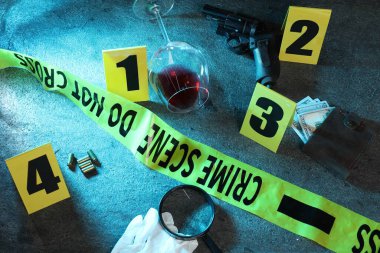 Adli tıp uzmanı. Sarı suç mahalli bandı, işaretler ve kanıtlar gri masada, üst tarafta.