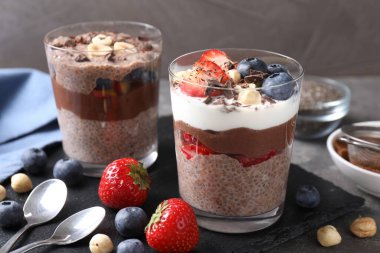 Chia tohumlu, fındıklı ve böğürtlenli lezzetli çikolatalı pudingler gri masada, yakın plan.