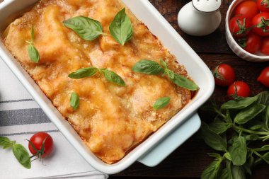 Pişirme kabında leziz vejetaryen lazanya ve ahşap masada malzemeler.