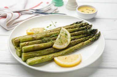 Beyaz ahşap masada limon ve kekik ile servis edilen lezzetli pişmiş kuşkonmaz, yakın plan.
