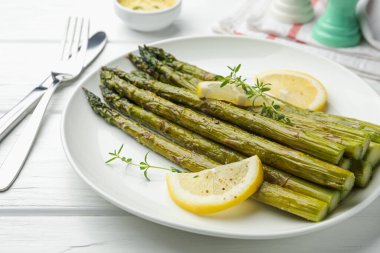 Beyaz ahşap masada limon ve kekik ile servis edilen lezzetli pişmiş kuşkonmaz, yakın plan.