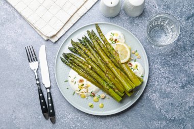 Lezzetli pişmiş kuşkonmaz, limon ve sosla servis edilmiş gri masa, düz.