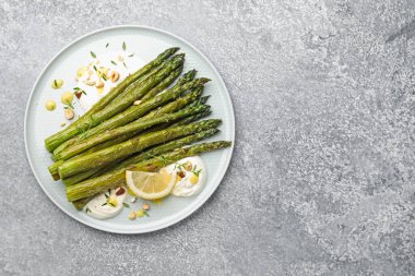 Gri masada limon ve sosla servis edilen lezzetli pişmiş kuşkonmaz. Metin için boşluk