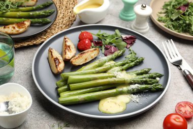 Lezzetli pişirilmiş kuşkonmaz fırında patates, domates ve sos ile servis edilir.