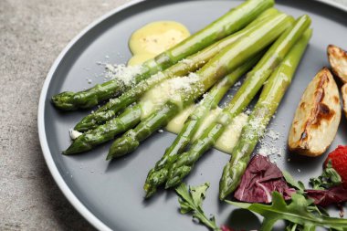 Lezzetli pişirilmiş kuşkonmaz fırında patates, domates ve sos ile servis edilir.