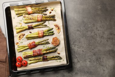 Pastırmalı, domatesli ve baharatlı kuşkonmaz pişirilmiş. Gri masa, üst manzara. Metin için boşluk