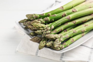 Beyaz ahşap masada taze çiğ kuşkonmaz mızrakları, yakın plan.