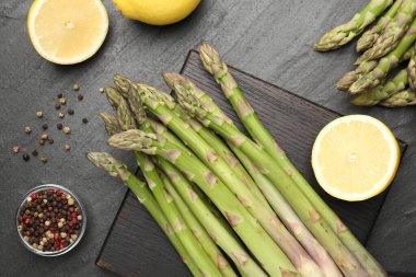 Taze çiğ kuşkonmaz mızrakları, limon ve baharatlar siyah masada, düz yerde.