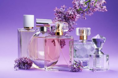 Parfümlü şişeler ve mor arkaplanda leylak çiçekleri, yakın plan.