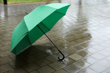 Islak asfaltta yeşil şemsiye, sağanak yağmur altında, yakın çekim. Metin için boşluk