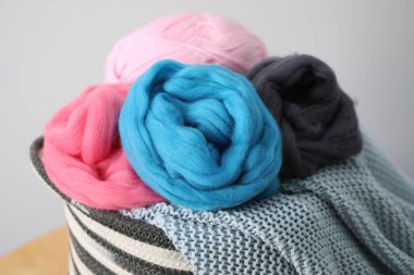 Yumuşak yün ve örgü ipliği sepetin içinde ahşap masada açık gri arka planda, yakın plan