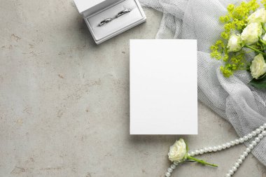 Düğün davetiyesi, gümüş yüzükler ve gri desenli masa üzerindeki çiçekler, düz yatak. Metin için boşluk