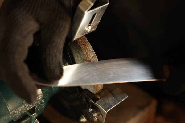 Man sharpening knife with bench grinder indoors, closeup