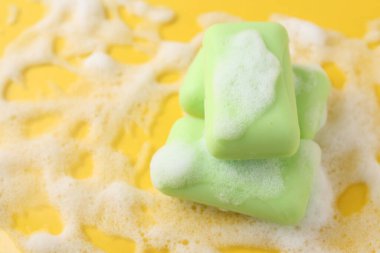 Sarı arka planda köpüklü sabun çubukları, üst tarafta. Metin için boşluk