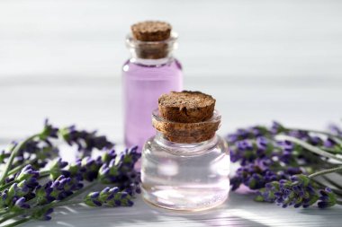 Beyaz ahşap masada doğal yağ ve lavanta çiçekleri, yakın plan.
