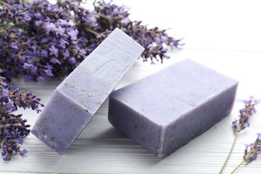 Sabun barları ve lavanta çiçekleri beyaz ahşap masada, yakın plan.