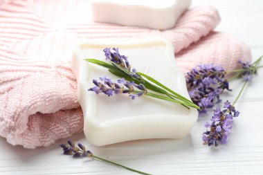 Sabun çubuğu, lavanta çiçekleri ve beyaz ahşap masa üzerindeki havlu, yakın plan.