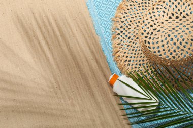 Plaj havlusu, hasır şapka, güneş kremi ve dışarıda kum üzerinde palmiye yaprağı. Metin için boşluk