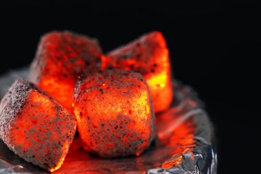 Siyah arkaplana karşı folyo kaplı nargile tutacağı üzerinde yanan kömür küpleri, yakın plan