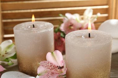 Yakıcı mumlar, taşlar ve zambak çiçekleri ahşap masada, yakın plan