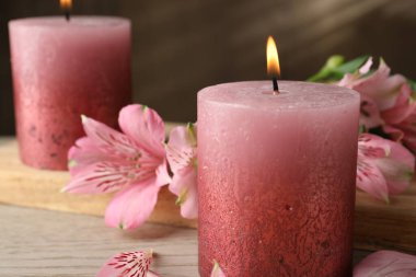 Beyaz ahşap masada yanan mumlar ve zambak çiçekleri, yakın plan.