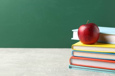 Farklı kitaplar ve gri masada kırmızı elma tahtaya karşı, yakın plan. Metin için boşluk