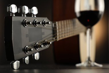 Akustik gitar ve bir bardak kırmızı şarap siyah masada, yakın plan.