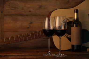 Akustik gitar, şişe ve kırmızı şarap bardakları ahşap masada. Metin için boşluk