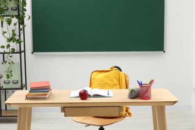 Farklı okul kırtasiyesi ve kırmızı elma, kapalı alanda tahtaya yakın ahşap masada.