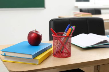 Farklı okul kırtasiyesi ve ahşap masada kırmızı elma.