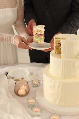 Damat, düğün pastasından bir parça tabağa koyuyor. Gelini masada kapalı tutuyor, yakın plan.