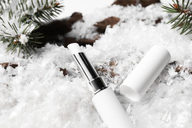 Nemlendirici dudak kremi ve suni kar üzerinde köknar ağacı dalları, yakın plan. Kış bakımı