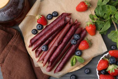 Lezzetli meyve dürümleri, çilekler, yaban mersinleri ve nane şekeri gri ahşap masada, düz uzanmış