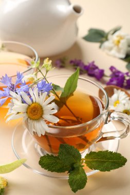 Cam fincanlarda aromatik bitki çayı, farklı çiçekler, bej arka planda nane ve çaydanlık, yakın plan