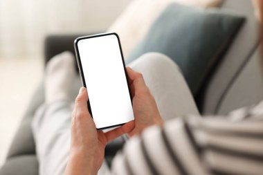 Evdeki koltukta modern akıllı telefon kullanan bir kadın.