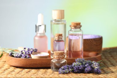 Hasır masanın üzerinde lavanta yağı ve çiçek şişeleri, yakın plan.