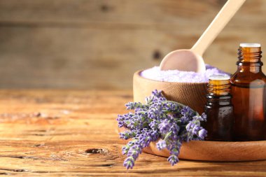 Lavanta yağı şişeleri, ahşap masada deniz tuzu ve çiçekler, yakın plan. Metin için boşluk
