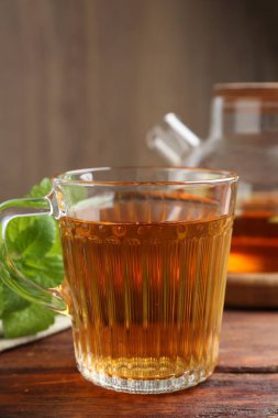 Cam fincanda aromatik limon merhemi çayı, çaydanlık ve ahşap masada taze yapraklar, yakın plan.