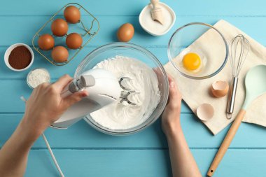 Açık mavi ahşap masada el çırpıcı kremalı bir kadın.