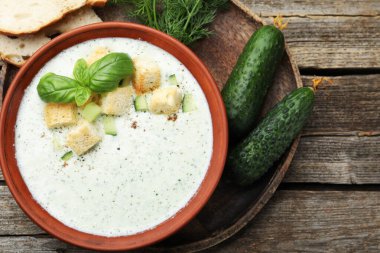 Lezzetli salatalık çorbası, kızarmış ekmek, fesleğen, ekmek ve sebzeler ahşap masada, düzlük.