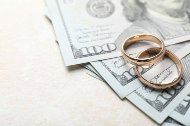 Beyaz masada iki altın alyans ve bir dolarlık banknotlar, yakın plan. Metin için boşluk