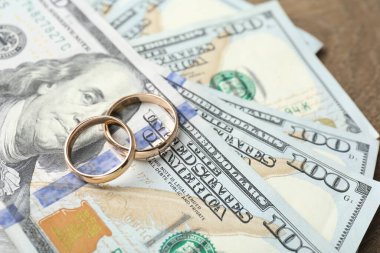 Altın alyanslar ve dolar banknotları ahşap masada, yakın plan.