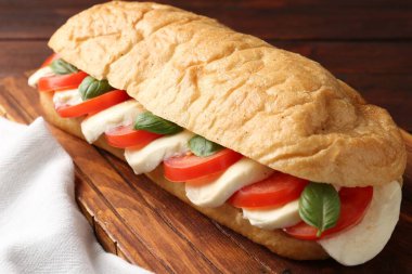 Mozarella peynirli, domatesli ve ahşap masadaki fesleğenli lezzetli sandviç.