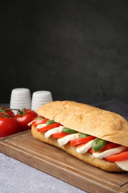 Mozarella peynirli, domatesli ve fesleğenli lezzetli sandviç. Gri desenli masa, koyu arkaplanlı, yakın plan. Metin için boşluk