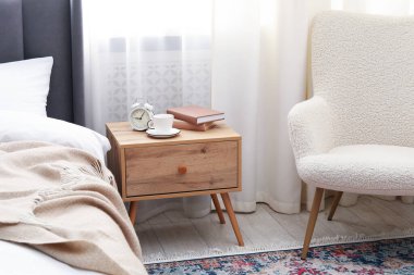 Yatağın yanında kahve, kitap ve çalar saat olan komodinin yanında.
